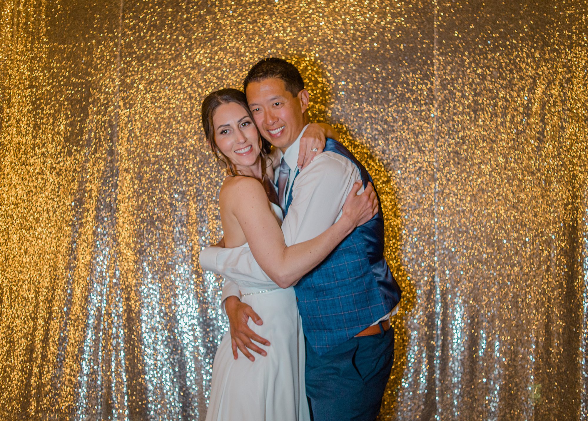 newlyweds hug in front of a gold background at Morgan Run Club & Resort Wedding