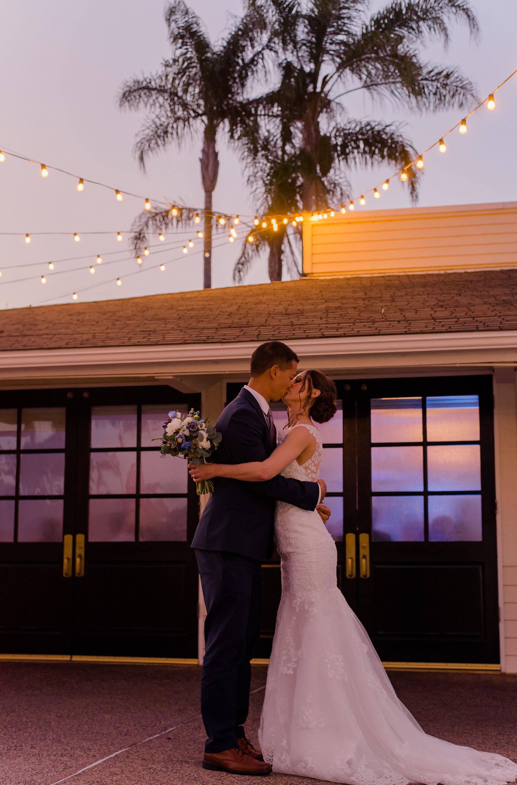 newlyweds kiss under the twinkling lights and evening sky