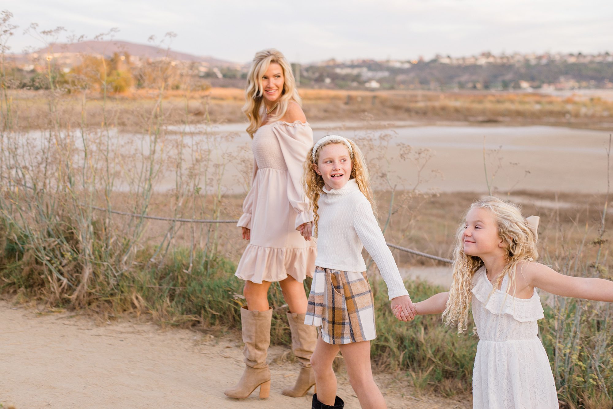 daughters hold hands with their mom as they walk along trail in Carlsbad CA