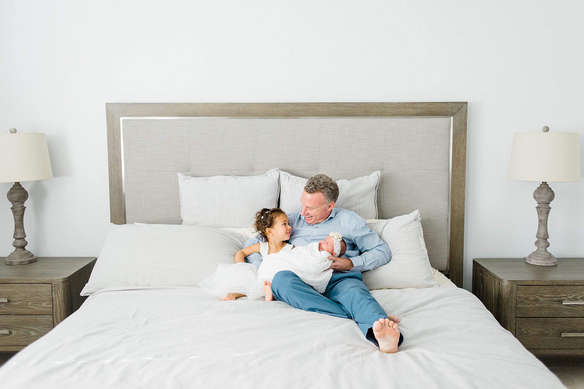 dad sits on bed holding his two daughters during San Diego In-Home Newborn Session