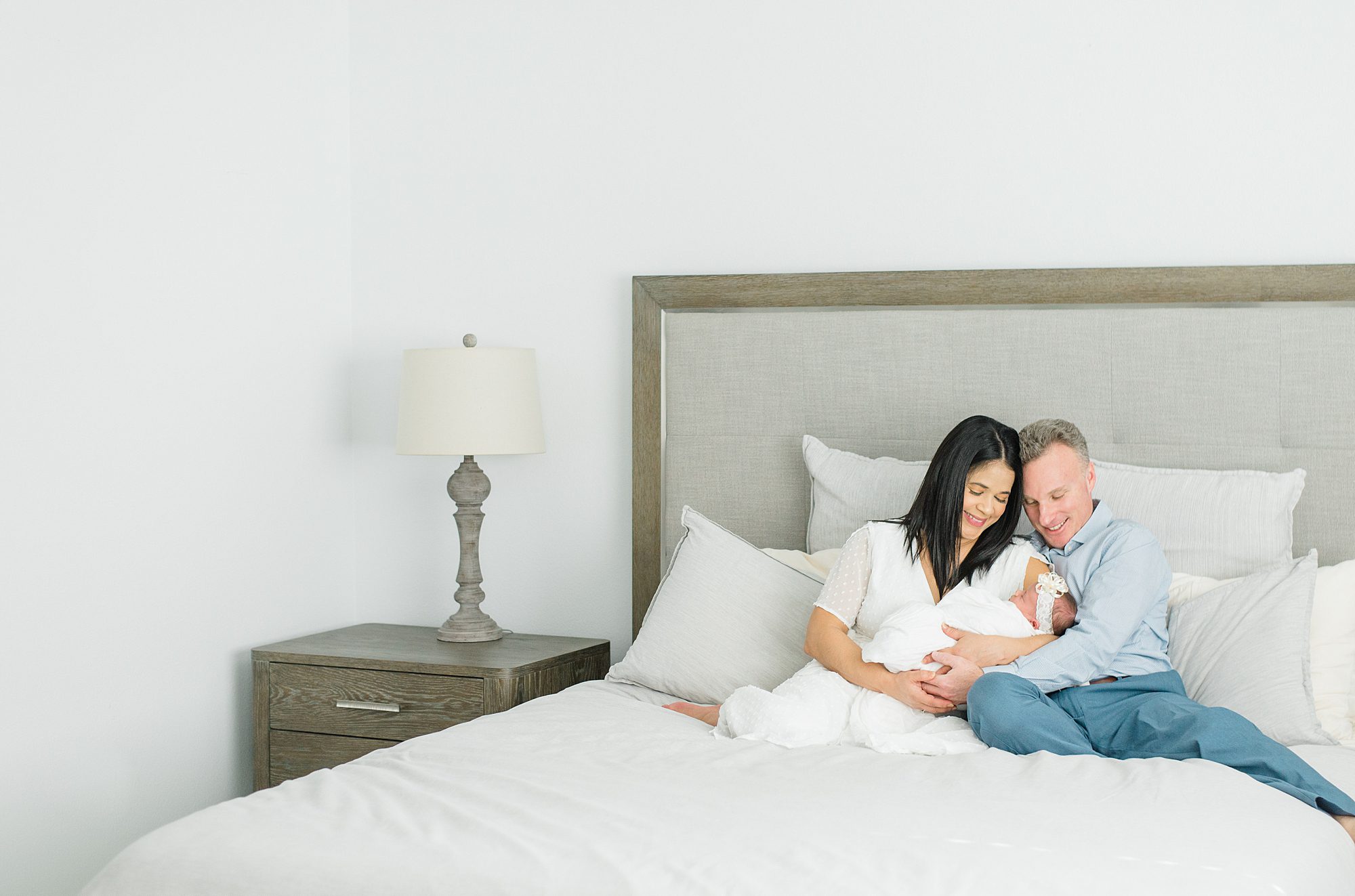 parents hold newborn girl sitting in bed during In-Home Newborn Session