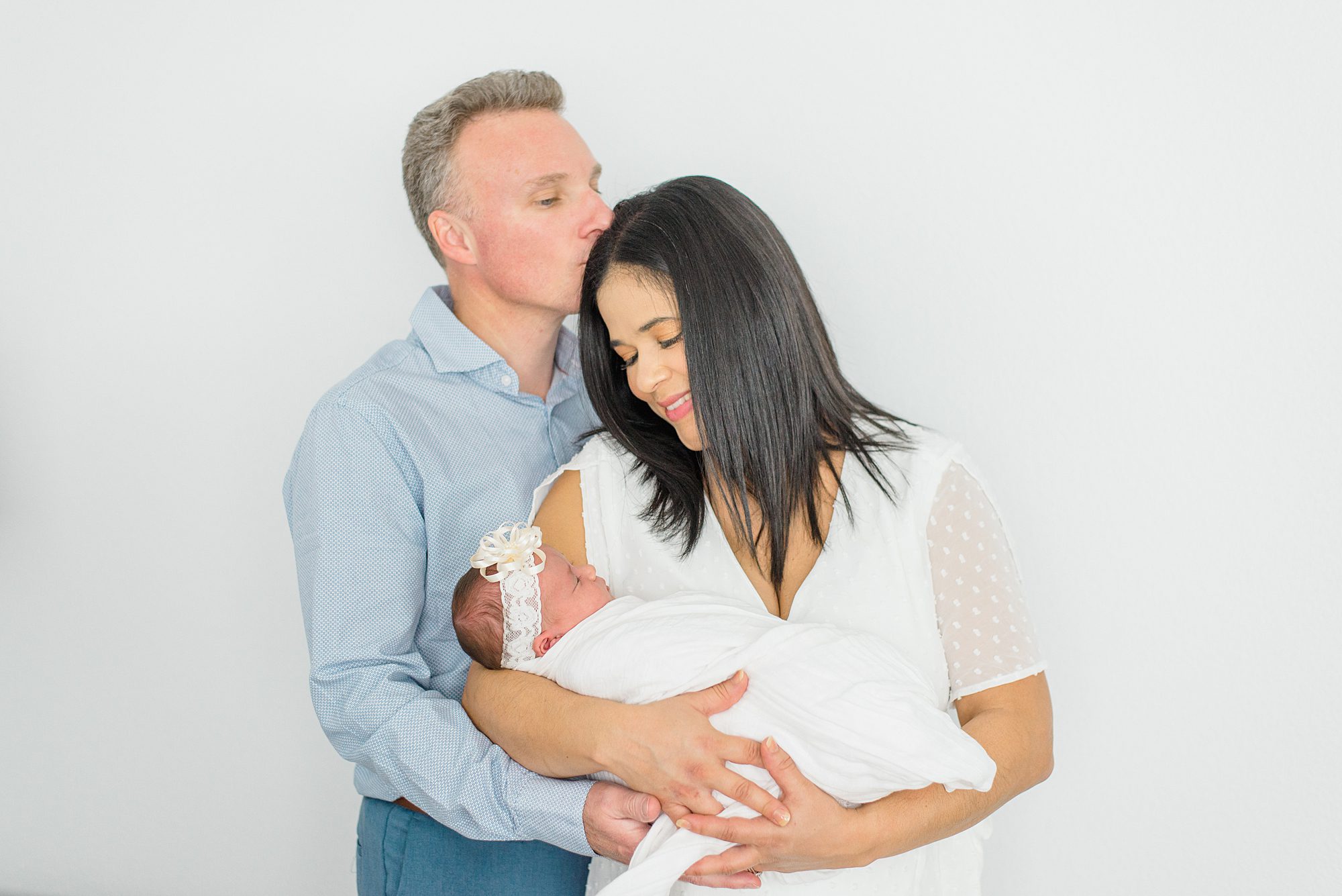 husband kisses wife's head while she holds newborn