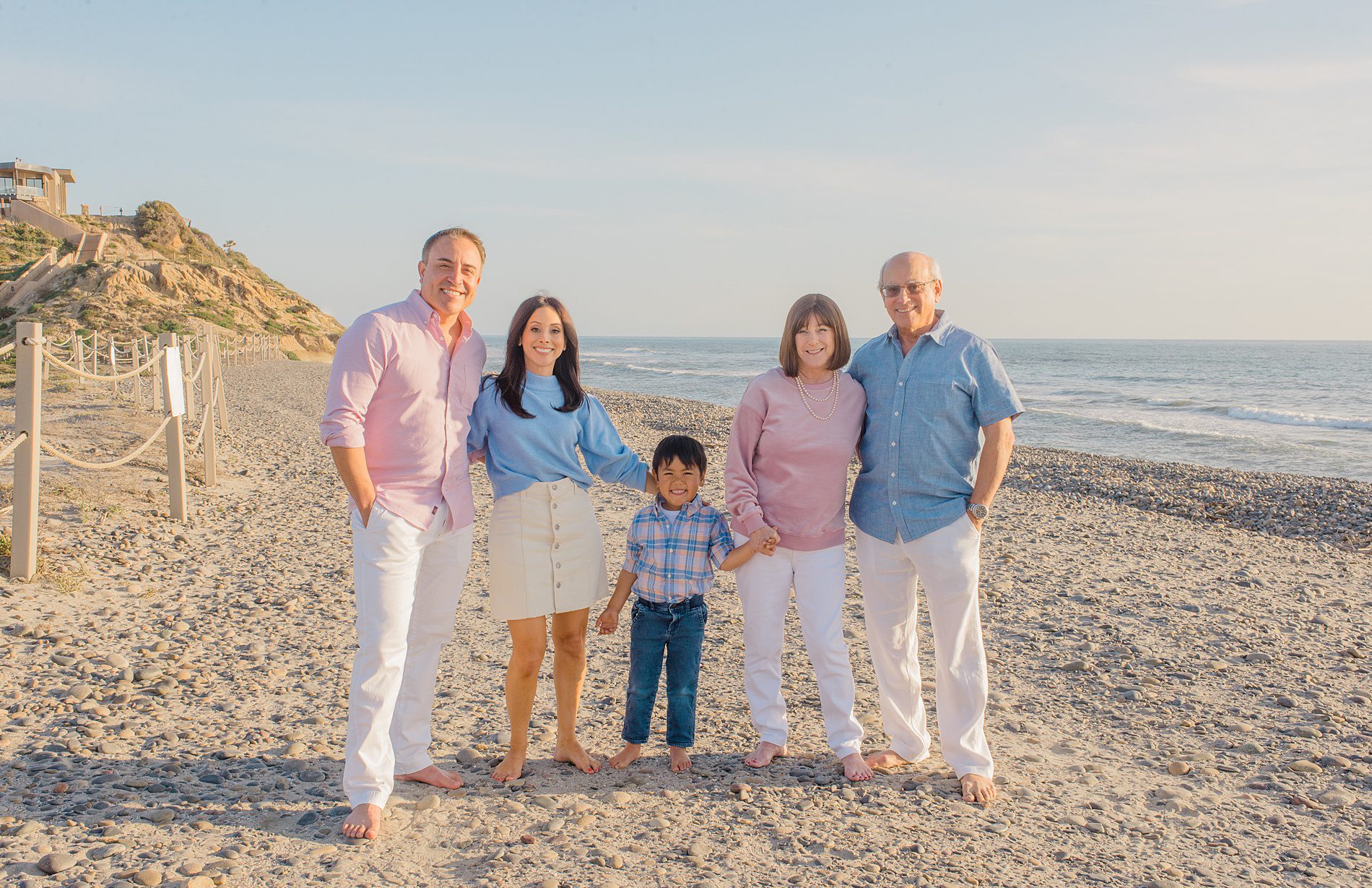 family of three and grandparents hold hands on beach for Coastal Family Portraits in Carlsbad California 
