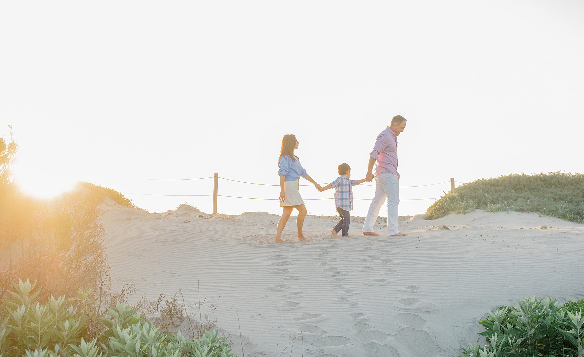 family of three walks along the beach as the sun sets photographed by San Diego Family photographer 