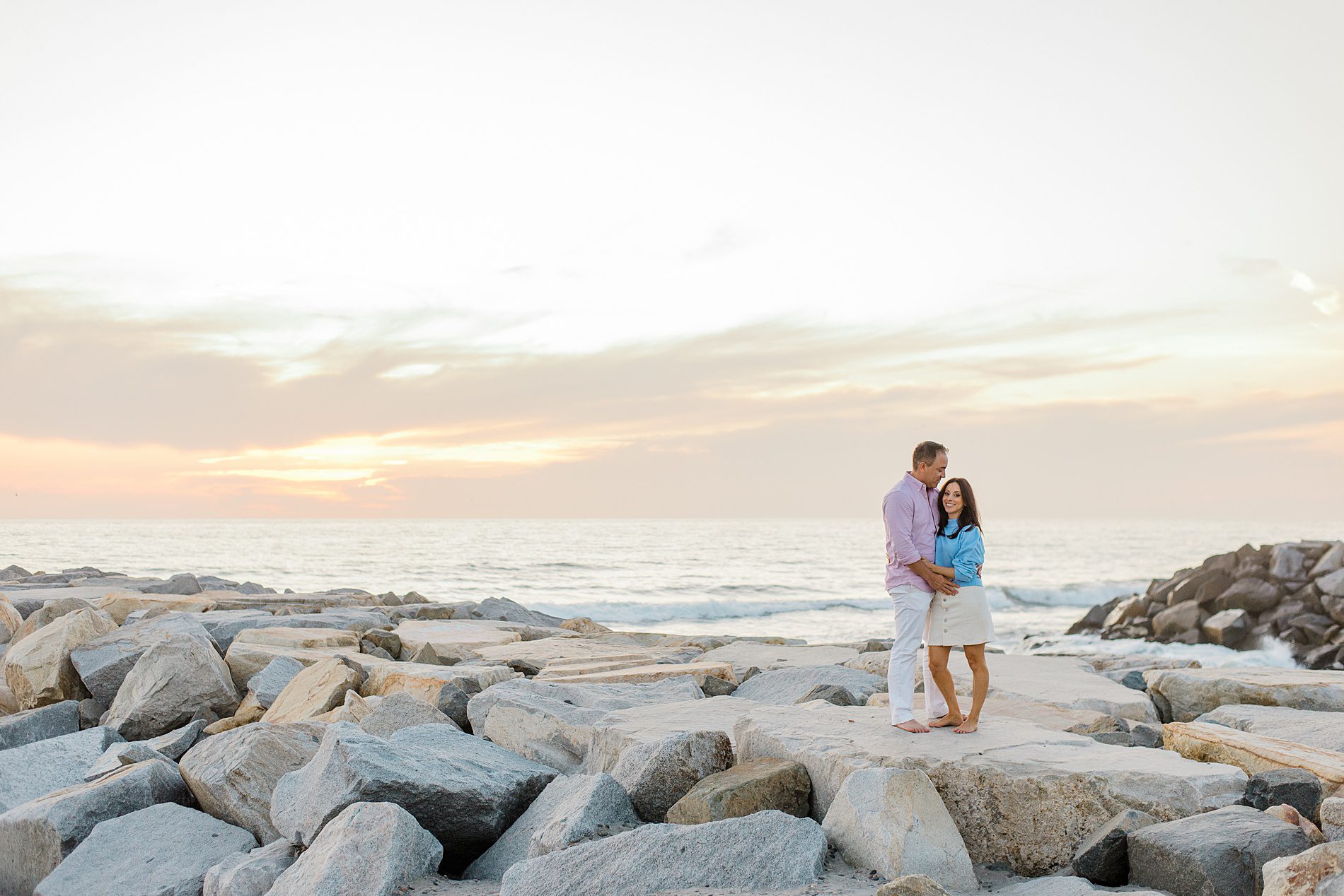 husband and wife stand together on rocks of coastline in Carlsbad California photographed by San Diego Family photographer 