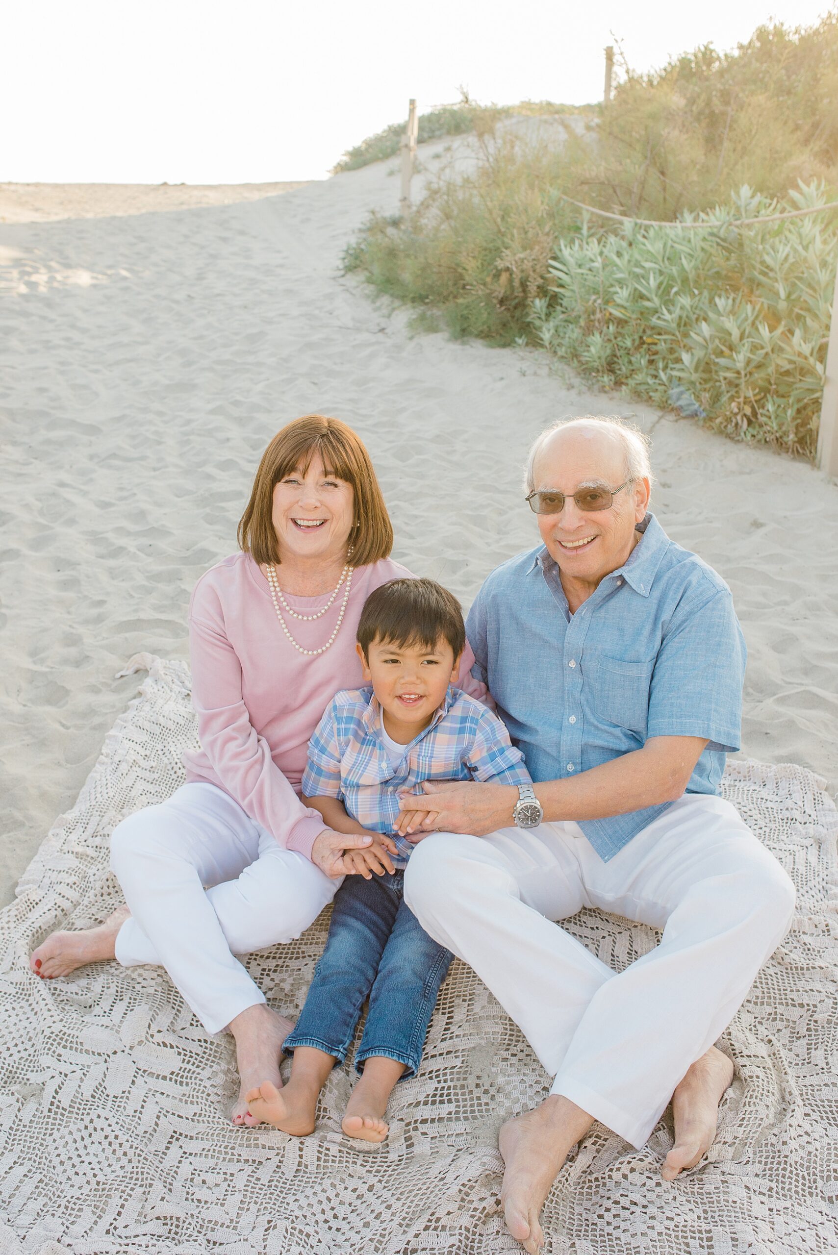 grandparents sit in the sand with their grandson