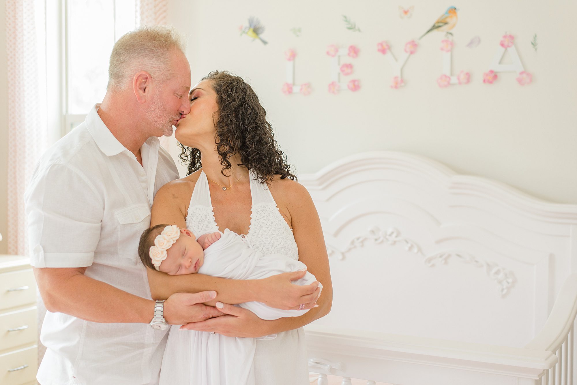 new parents kiss as they hold their newborn daughter 