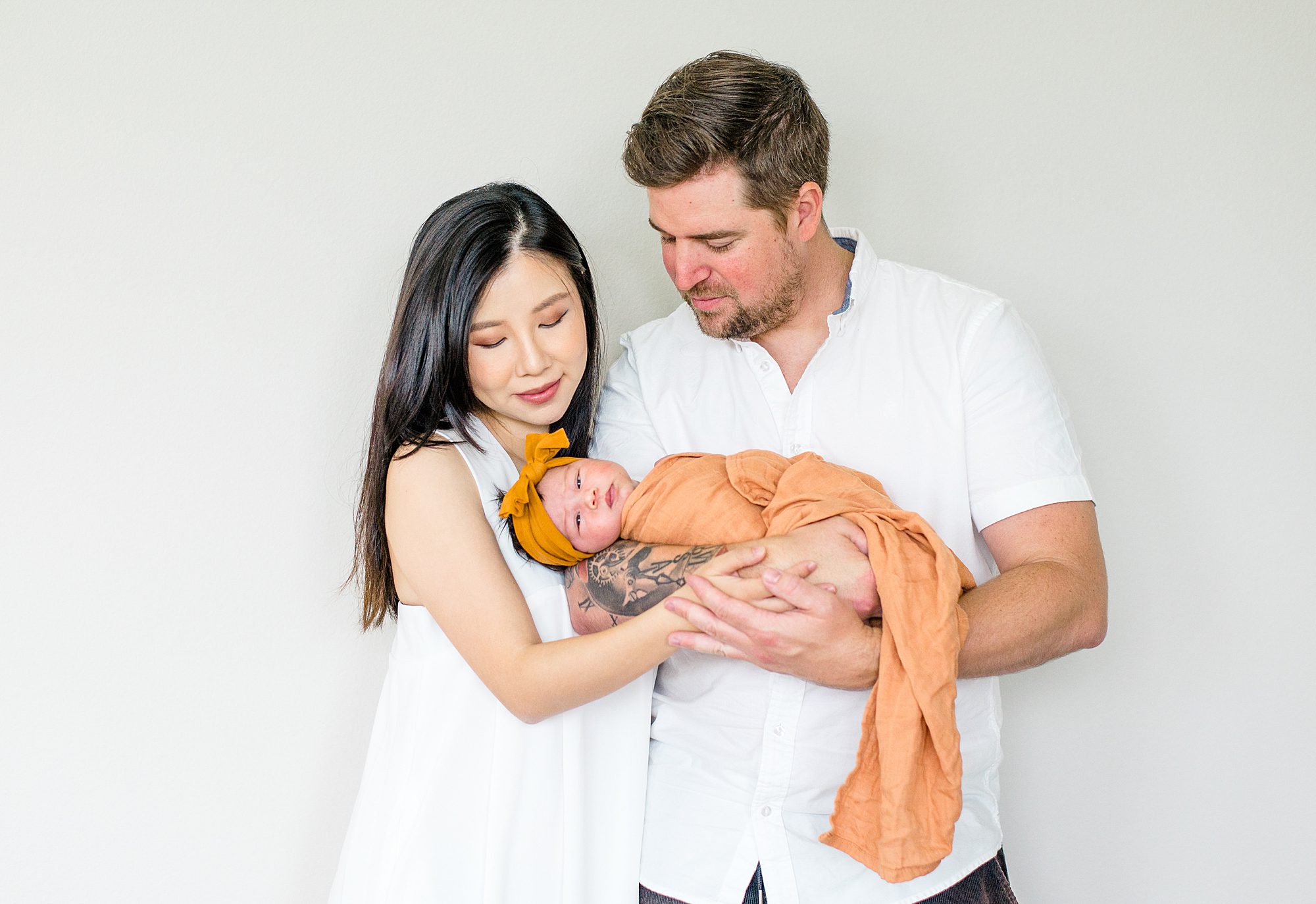 parents look at their baby girl wrapped in a mustard yellow blanket and headband