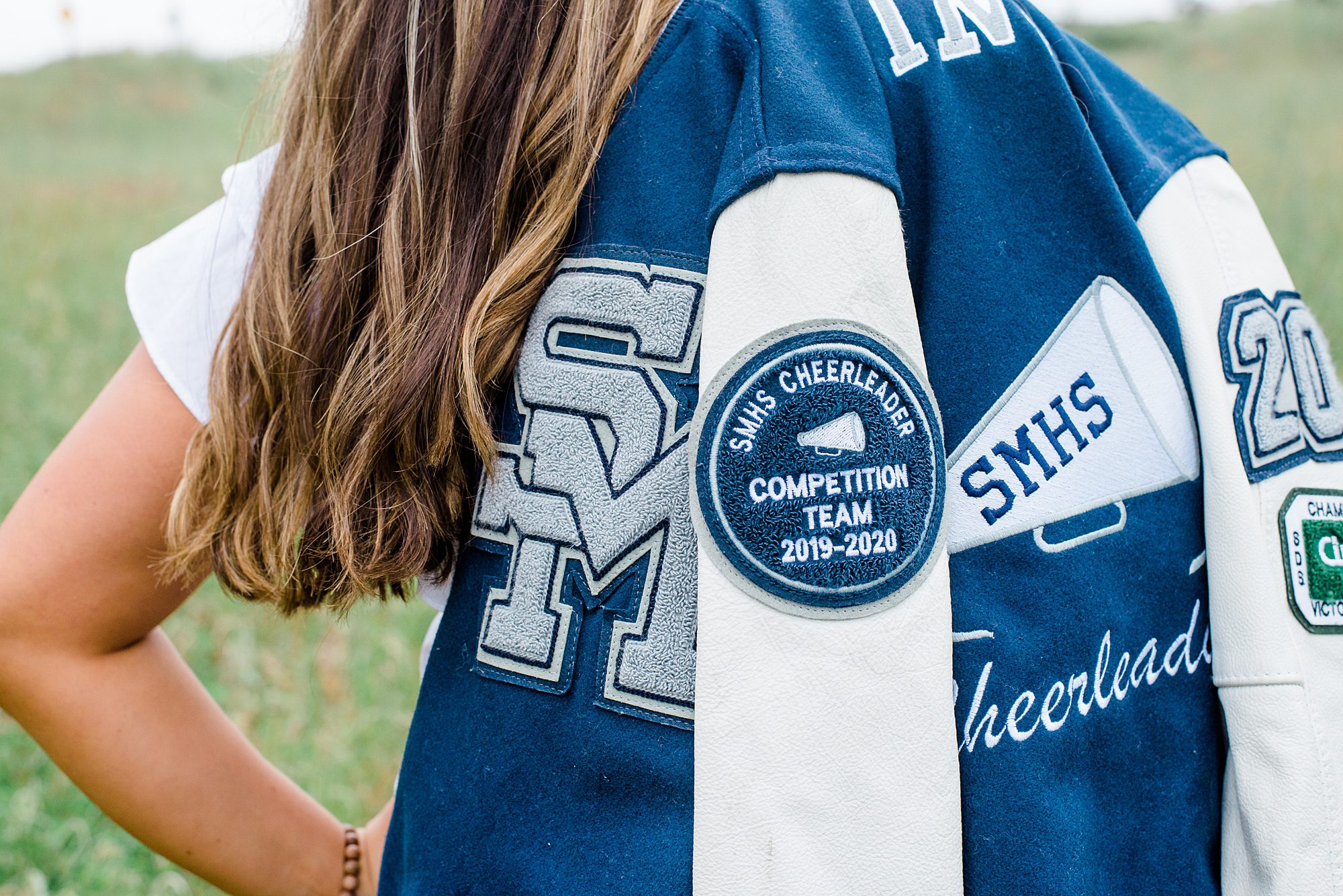 senior girl showing off competitive cheer patches on jacket