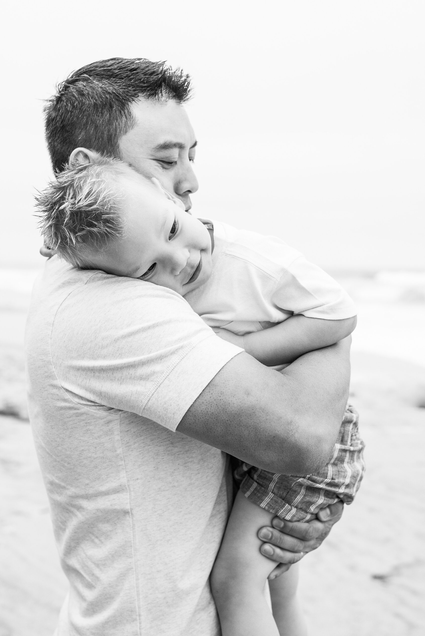 dad holds his son during timeless family portaits on beach