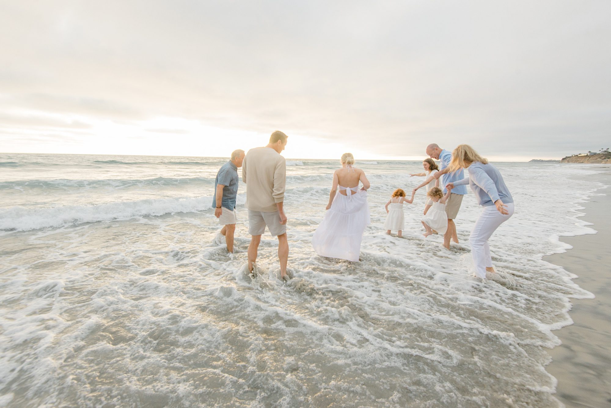 family of 8 splashes in the ocean waves during San Diego beach session