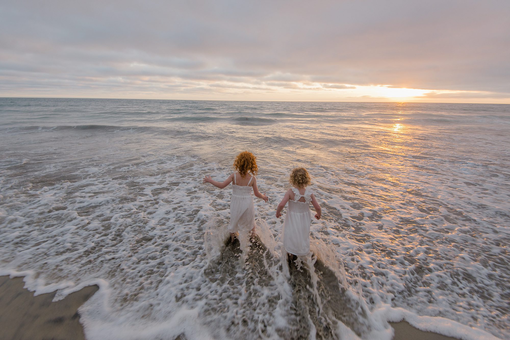 sisters run into the ocean waves in San Diego 