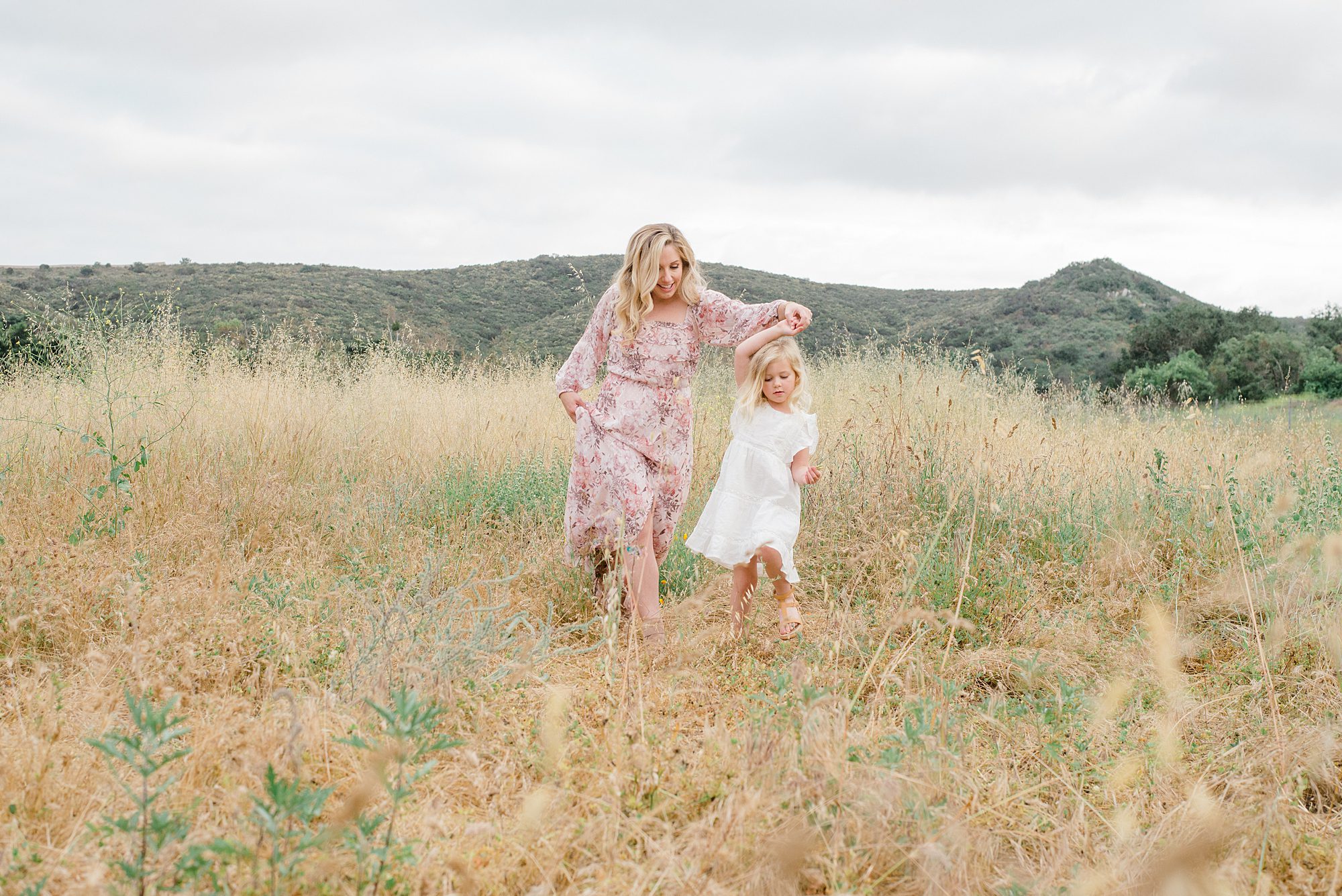 mom and daughter walk together through field 
