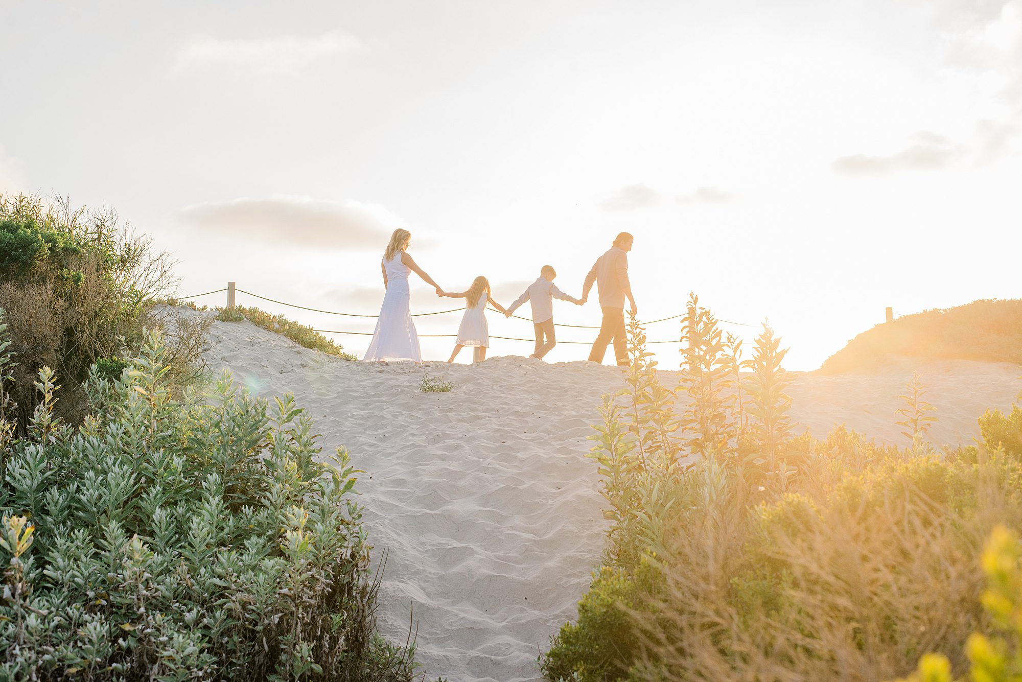 family walks along sand dunes at sunset
