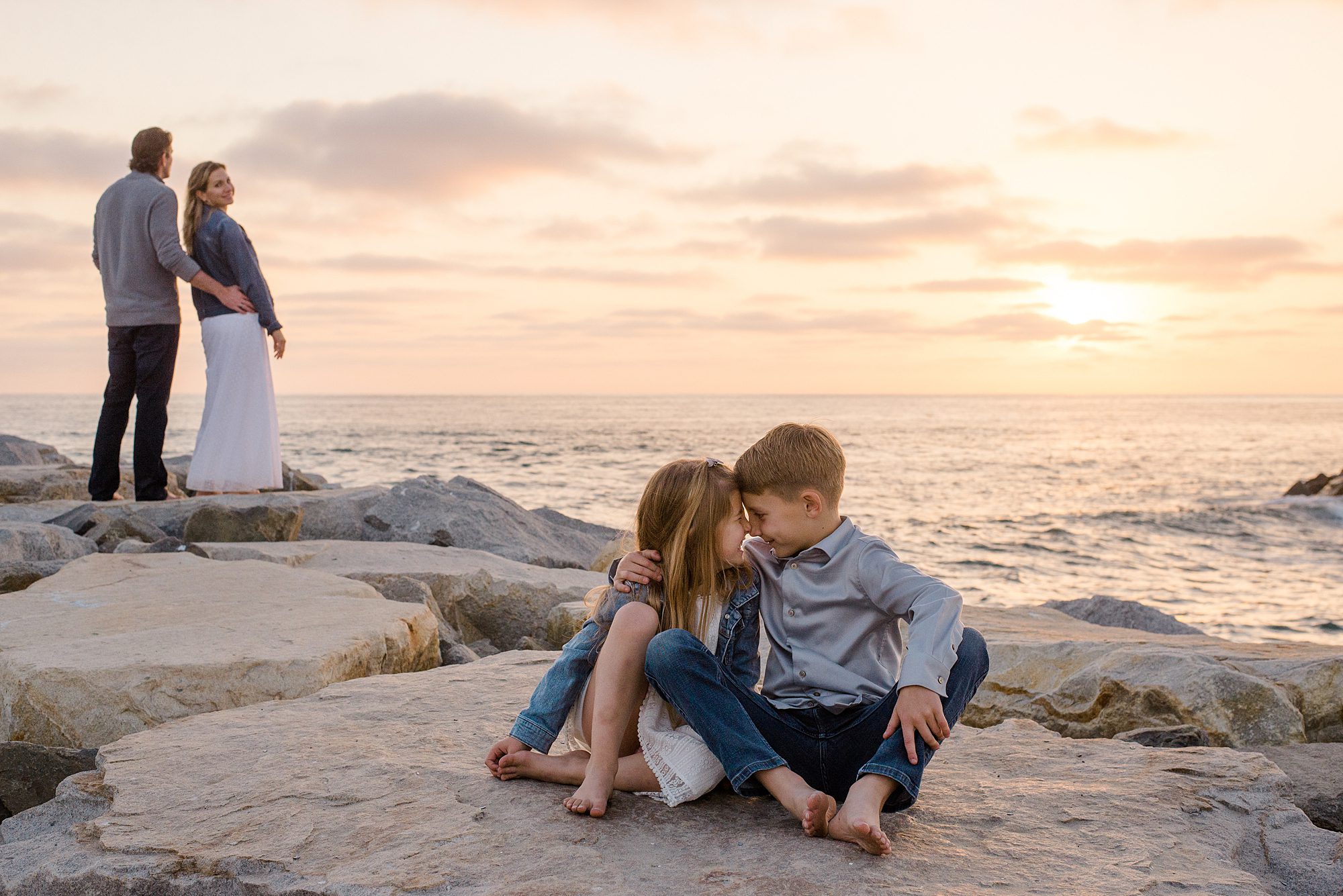 siblings sit together as parents look out at the ocean