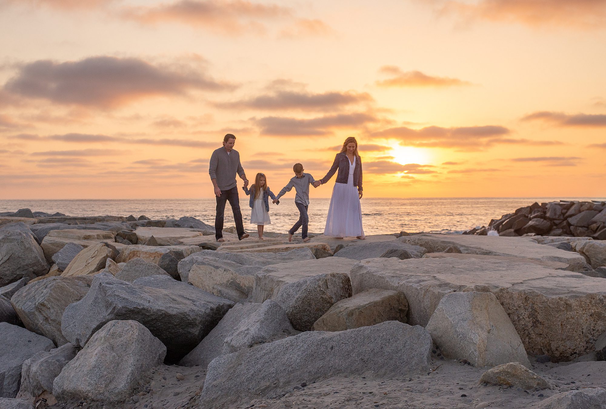 family walk along the jetty during family beach portraits in Carlsbad, CA 