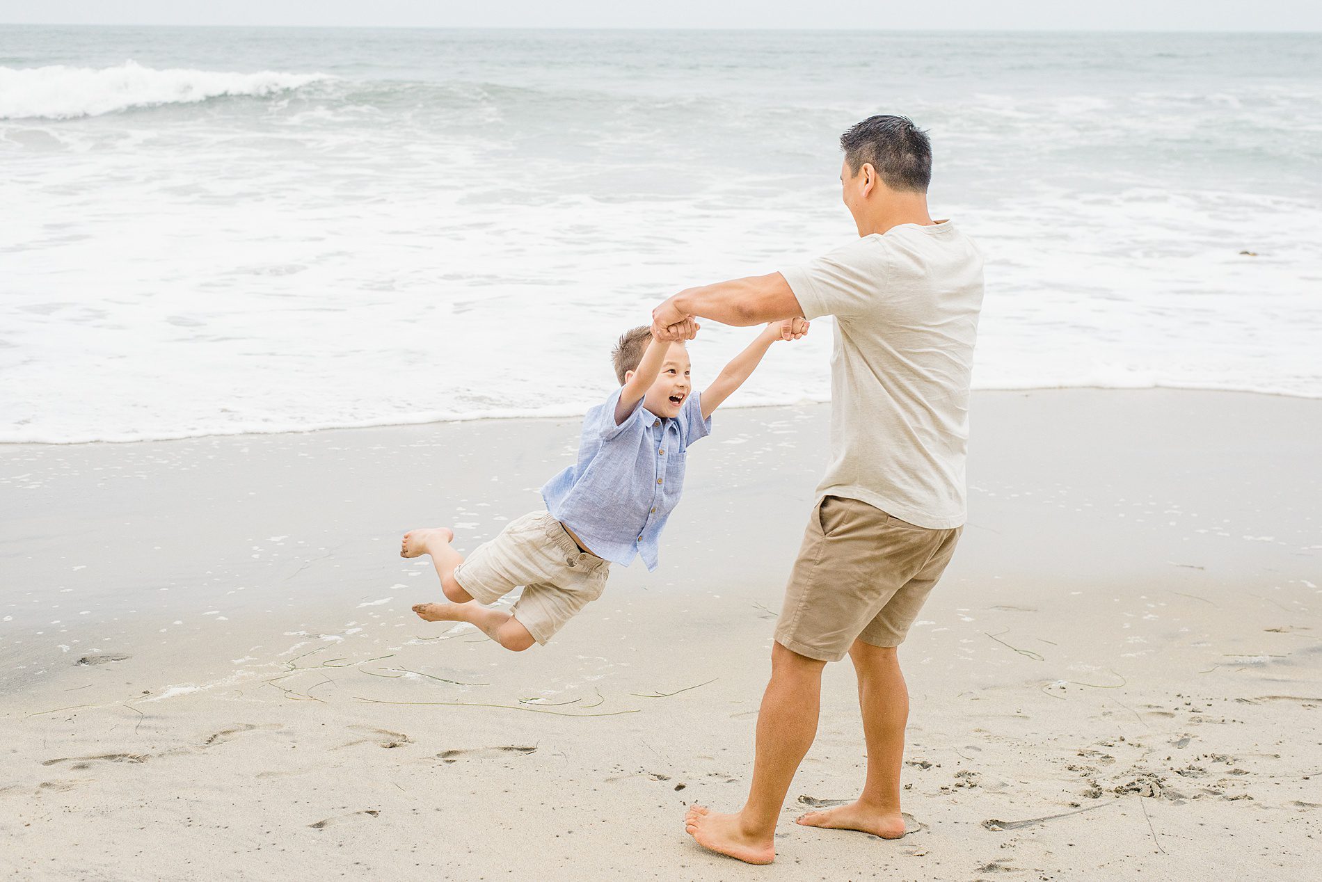 dad swings his son around on the beach 