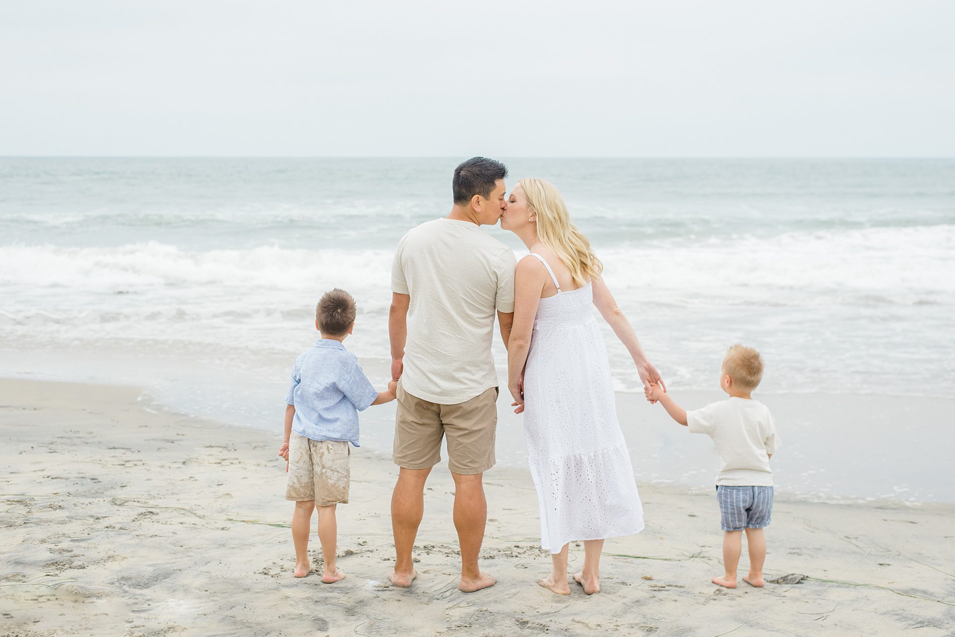 couple kiss holding their sons' hands during San Diego Family Beach Session