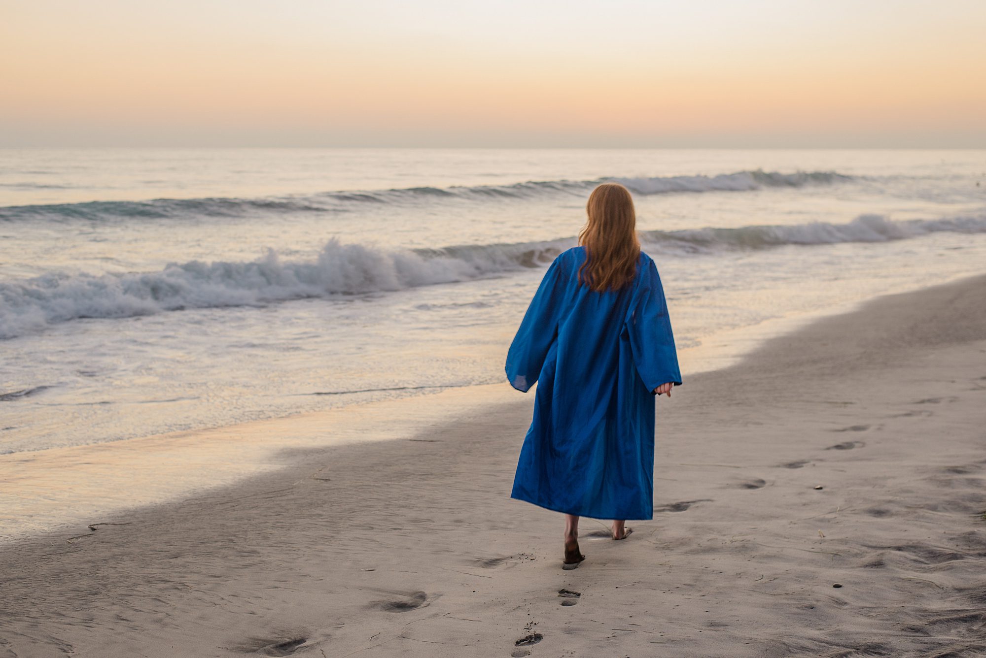 senior walks along the beach in cap and gown