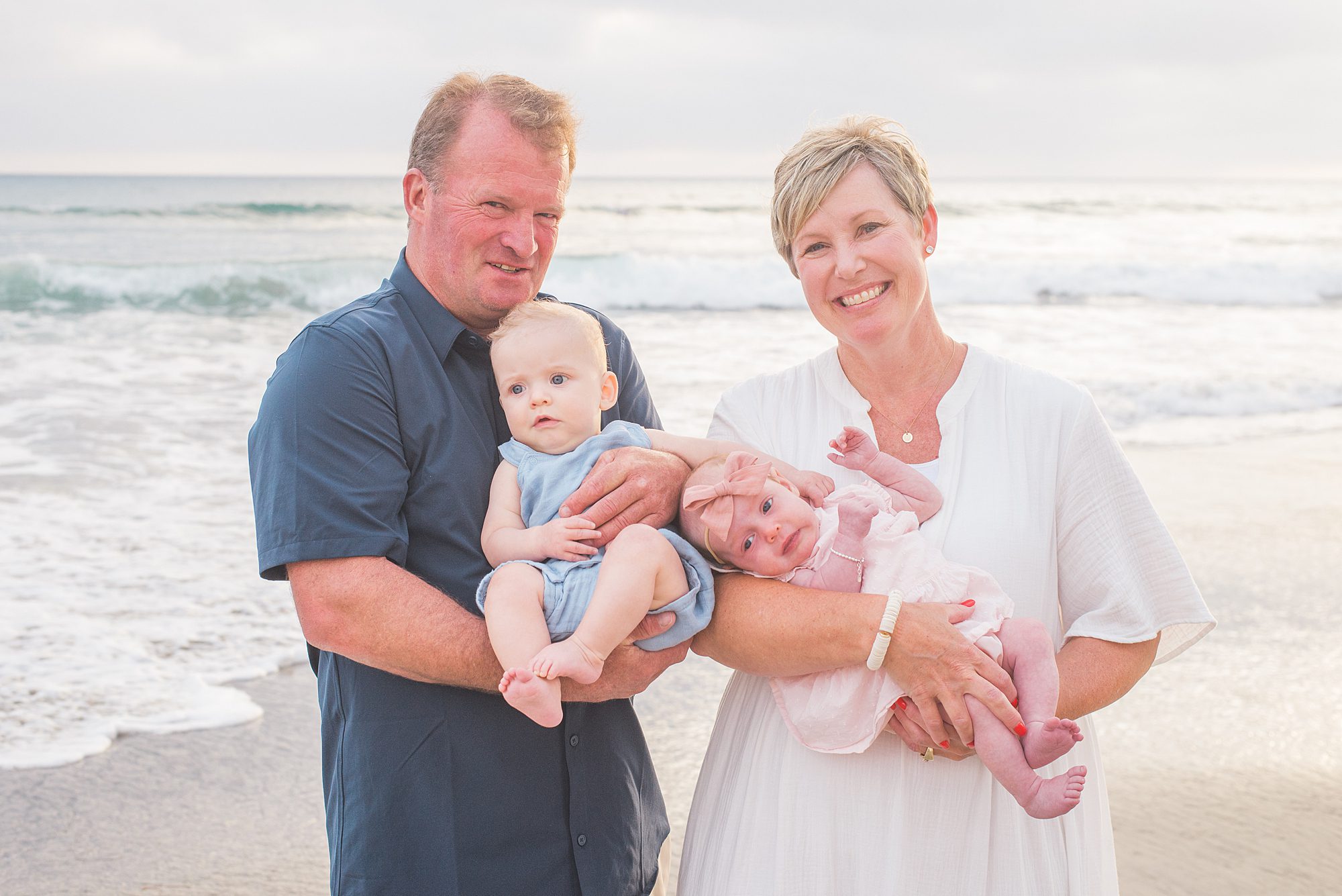 grandparents hold their two grandchildren on the beach